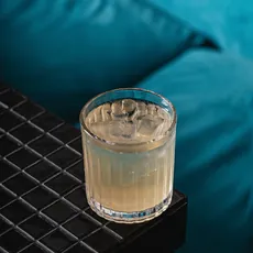 Copo de Alvorada sobre mesa de ladrilho preto, sofá turquesa ao fundo