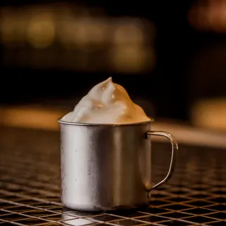 Caneca de metal gelada com espuma de gengibre no topo, servida no balcão do bar