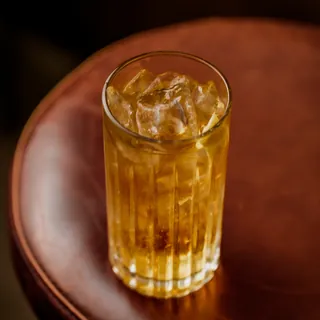 Copo alto do drink Caju Highball com gelo, sobre banqueta de couro