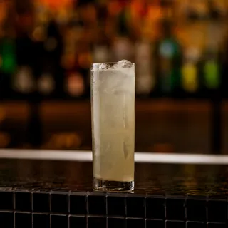 Copo alto do drink Refresco no balcão, com as garrafas do bar ao fundo