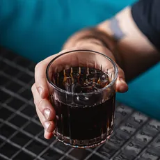 Copo de Reset com o drink âmbar-avermelhado, sofá turquesa ao fundo